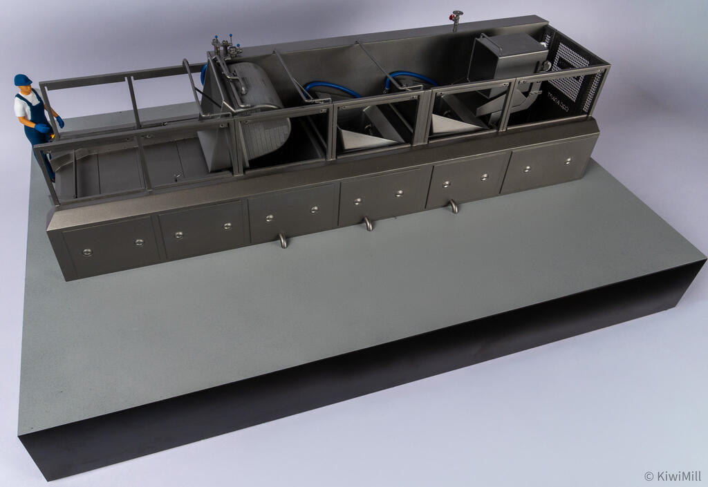 High angle of the cooking line model from the loading end, with valve fittings atop the curved cooking basket
